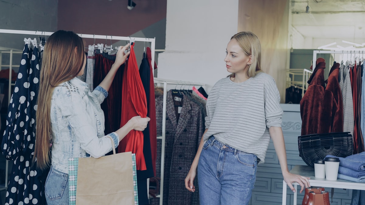 Two women smiling and choosing clothes together in a boutique.